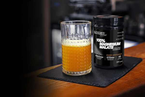 Magnézium Malát blenie vedľa skleneného pohára s nápojom Magnézium malát orandzovej farby kvôli pomarančovej príchuti na kamennom podnose a drevenom stole.